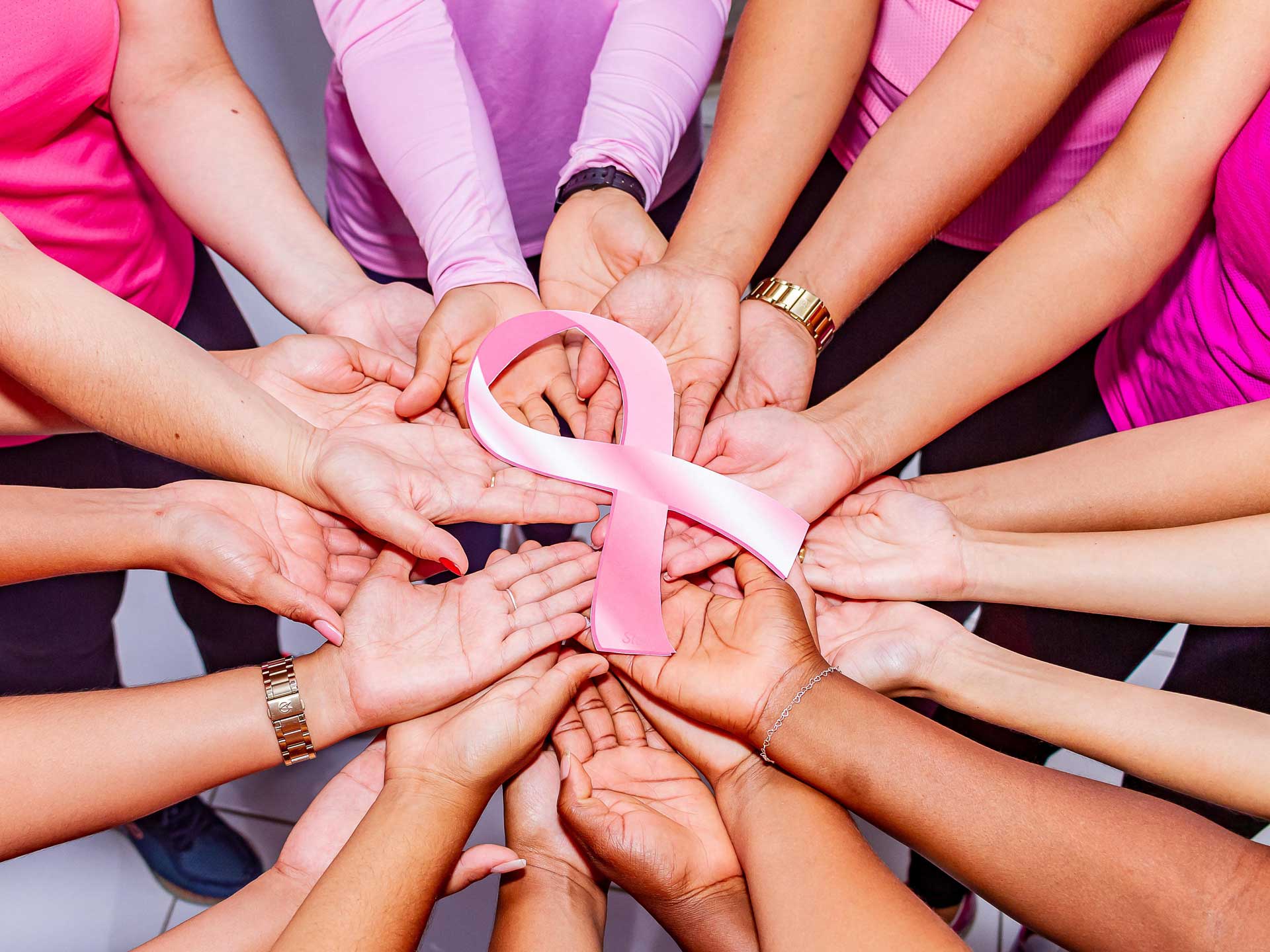 many womens hand reaching into the centre of a circle holding a breast cancer ribbon
