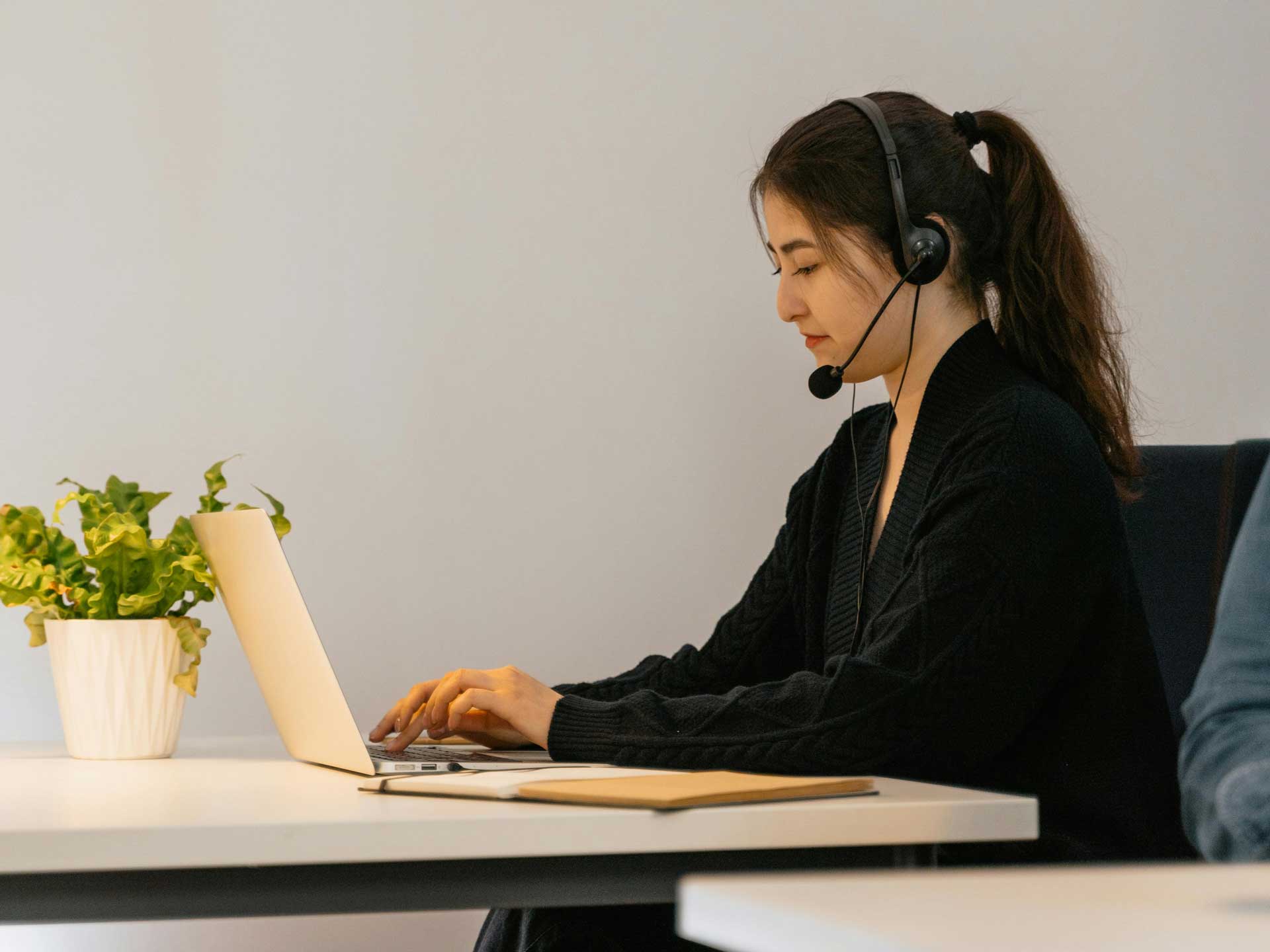 A young woman sitting at a desk with a laptop while wearing a headset